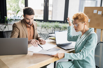 Obraz premium bearded manager pointing at document near displeased businesswoman in office.