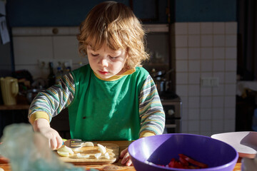 A little boy cuts an onion in the kitchen
