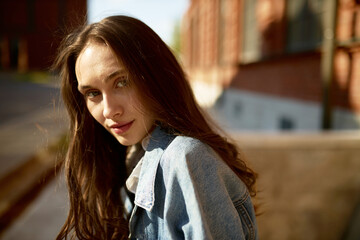 Human appearance. Portrait of charming adorable beautiful young woman of 20s with long beautiful hair looking at camera strolling around city in denim outfit. Womenswear, female fashion