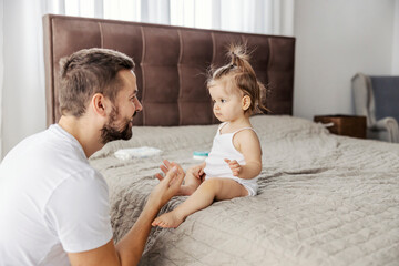 A cheerful dad is talking to his baby girl and teaching her how to talk.