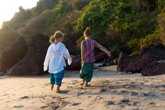 Two hippie girls walking by the sand on tropical beach. Ocean coast, Arambol, India