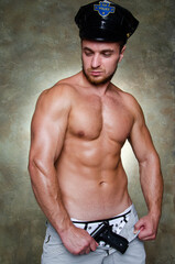 Young handsome stripper posing in the studio. A man with an athletic body dressed as a police...
