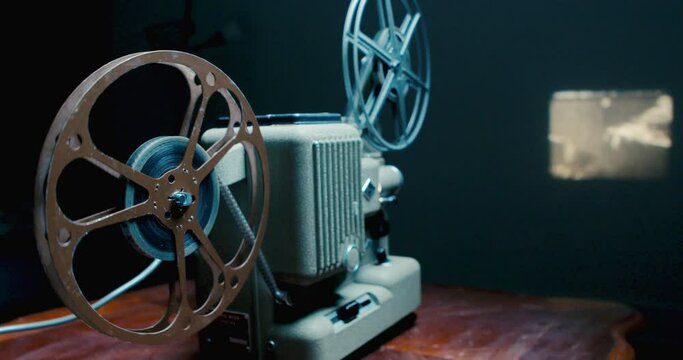Closeup of an Old 8mm Movie Projector Shows a Film in a Dark Room. Vintage Film, Old Cinema Concept. Old fashioned retro cinema projector plays film on the rooms with furniture and lamp.