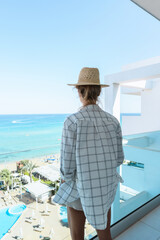 Woman wearing straw hat enjoy view from balcony of beachfront hotel or apartment
