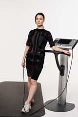 Fit girl in EMS suit on white background. Fitness girl trainer before workout in EMS suit. Sport...