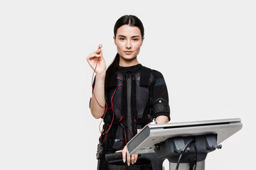 Fototapeta na wymiar Fit girl in EMS suit with contactor in hand that uses electrical impulses to stimulate muscles on white background. Sport training in electrical muscle stimulation suit.