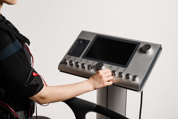Set up EMS device for workout sport training in electrical muscle stimulation suit on white background. Girl trainer is setting up EMS device before training.