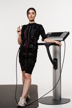 Fit girl in EMS suit with contactor in hand that uses electrical impulses to stimulate muscles on white background. Sport training in electrical muscle stimulation suit.
