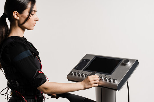 Girl trainer is setting up EMS device before training. Set up EMS device for workout sport training in electrical muscle stimulation suit on white background.