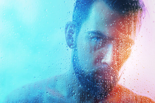 Portrait of handsome young man captured through wet glass in blue and orange light