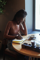 Portrait of young concentrated African-American woman with long dark braids wearing pink roll-neck...