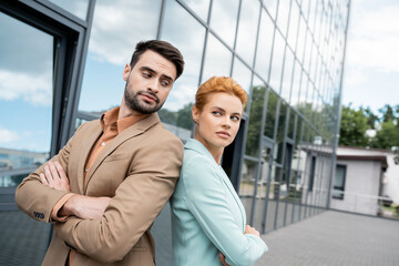 skeptical business people standing back to back with folded arms near building on city street.