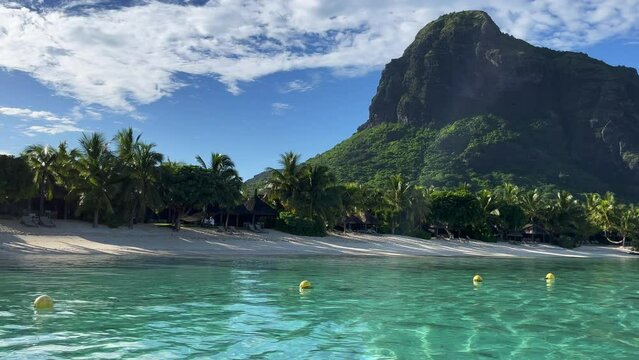 Le Morne beach, view from the the ship. Beautiful turquoise water and exotic nature. Tropical beach with palm trees and white sand blue ocean and beach beds with umbrellas and sun chairs.