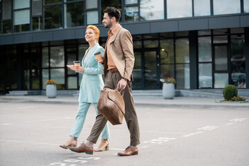 successful managers in fashionable suits walking with coffee to go on urban street.