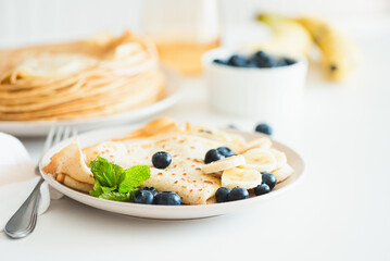 French crepes with banana and blueberries on white table. Copy space