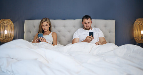Obraz na płótnie Canvas Id rather scroll than shout. Shot of a young couple using their phones separately after an argument in bed.