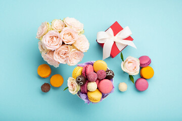 Macaroons, Gift Box, Rose Flowers and Chocolate Candies on Blue Background. Spring Presents Concept