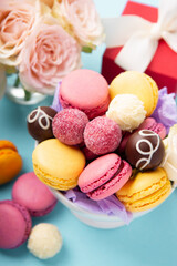 Macaroons, Gift Box, Rose Flowers and Chocolate Candies on Blue Background. Spring Presents Concept