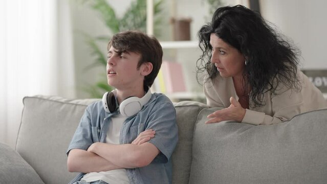 Woman giving advice to son and the teenager boy ignoring her putting on the headphones and starting to play video game