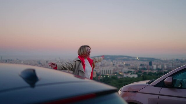 With sense of happiness and zest for adventure, young woman jumps for joy near rental car enjoying every moment of travel destination. Female tourist daces with joyful heart near the vehicle