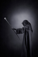 Wizard with hooded cape and magic staff over dark misty background