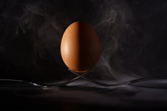 &oelig;uf pos&eacute; sur deux fourchettes avec fum&eacute;e sur fond noir