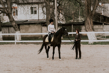 A woman instructor teaching girl how to ride a horse.  Female rider practicing on a horseback learning equestrian sport. Active lifestyle and leisure activity concep