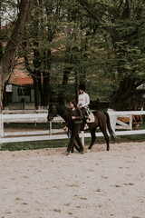 A woman instructor teaching girl how to ride a horse.  Female rider practicing on a horseback learning equestrian sport. Active lifestyle and leisure activity concep