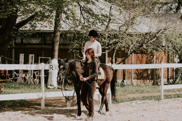 A woman instructor teaching girl how to ride a horse. Female rider practicing on a horseback learning equestrian sport. Active lifestyle and leisure activity concep