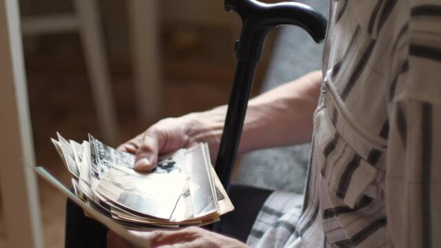a pensioner sitting with a walking stick examines family photos while inside. the concept of an elderly person remembers the past, nostalgia, melancholy, family tree