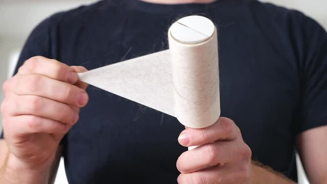 The guy removes hair and wool from the T-shirt with a lint roller. Man holding a hair removal roller.