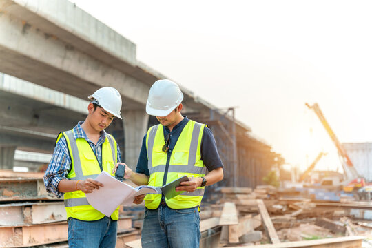 Apprentice And Civil Engineer Inspecting And Working Outdoors Road Construction Site With Blueprint And Tablet. Civil Engineer.