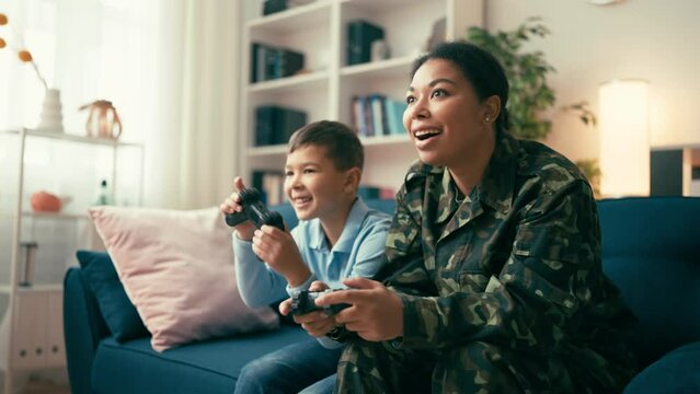 Military African American mom and her little son playing video game at home