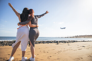 Two girls watch a plane land and are happy and hug each other