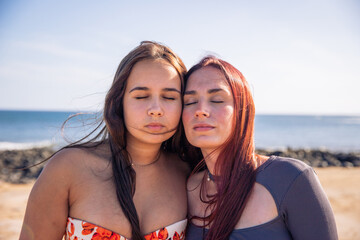 Two sisters pose with faces close and eyes closed at the beach, love between sisters
