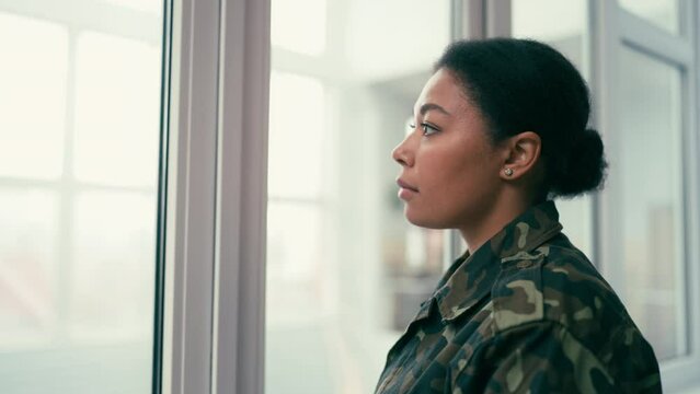 Sad African American soldier woman looking out the window, grieving, problems