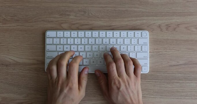 Male hands typing on a white keyboard using computer at workplace in office top view. IT employee works finger and internet search assistant