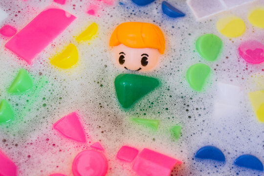 Washing of children toys, plastic building blocks with figurines. A smiling little fellow and colorful cubes float in the foaming water