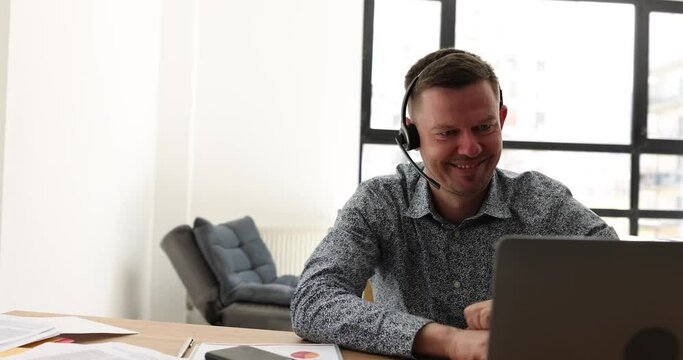 Smiling telemarketer sales agent on phone, wears wireless headset and conducts video conference on laptop. Happy manager talking and consulting online client