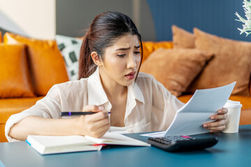 Upset asian woman sit at desk do accounting job or manage personal finances, reviewing bills feels...