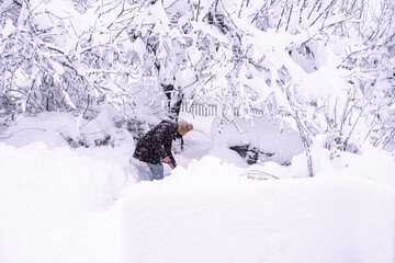 a woman shovels snow in the garden during a snowfall