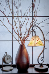 和室の障子の前に飾られた細かい枯れ枝とクラシカルな照明灯と時計