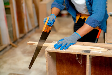 Close up hands of carpenter use saw to cut timber in wood factory or workplace.