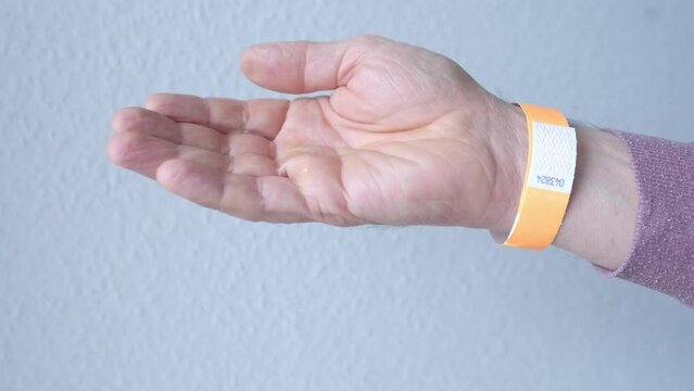 orange paper wristband mockup on persons arm. Clear adhesive bangle wristlet sticker with entry number on male hand of middle-aged european man, blue paper bracelet, check tape, event ticket concept