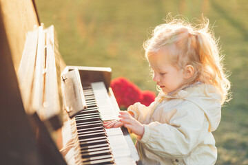 toddler blonde girl playing piano outside, exploring music instrument, performance, early childhood...