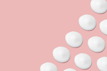 Lots of smears of cosmetic cream. Light, smooth surface. Texture of spreadable cream. Liquid creamy strokes. On a pink background. Cosmetic background, banner.