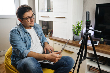 Hand free. Middle-aged male sitting at home before smartphone fixed on tripod. Video blogger...