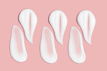 Lots of smears of cosmetic cream. Light, smooth surface. Texture of spreadable cream. Liquid creamy strokes. On a pink background. Cosmetic background, banner.