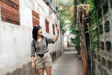 Fototapeta na wymiar Young Asian woman backpack traveler using mobile phone, enjoying street cultural local place. Traveler checking out side streets.