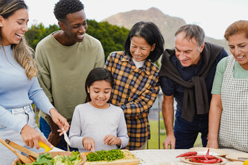 Happy multiracial people preparing dinner together at home terrace - Multi generational friends having fun cooking with little girl outdoor